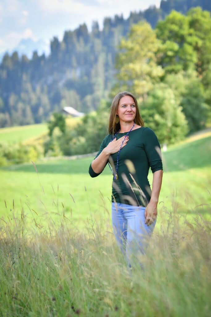 Achtsamkeit in der Natur – Outdoor Coaching mit Mareile Poettering Frau steht achtsam in einer Wiese mit Hand auf dem Herzen – Naturcoaching mit Mareile Poettering im Allgäu