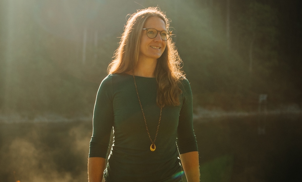 Frau steht im warmen Morgenlicht in der Natur und lächelt sanft