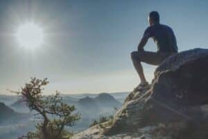 Mann auf einem Felsen mit Blick in die Weite der Berge, Symbol für Orientierung, Klarheit und innere Präsenz.