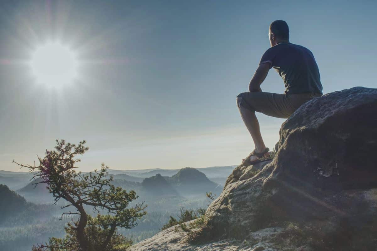 Mann auf einem Felsen mit Blick in die Weite der Berge, Symbol für Orientierung, Klarheit und innere Präsenz.